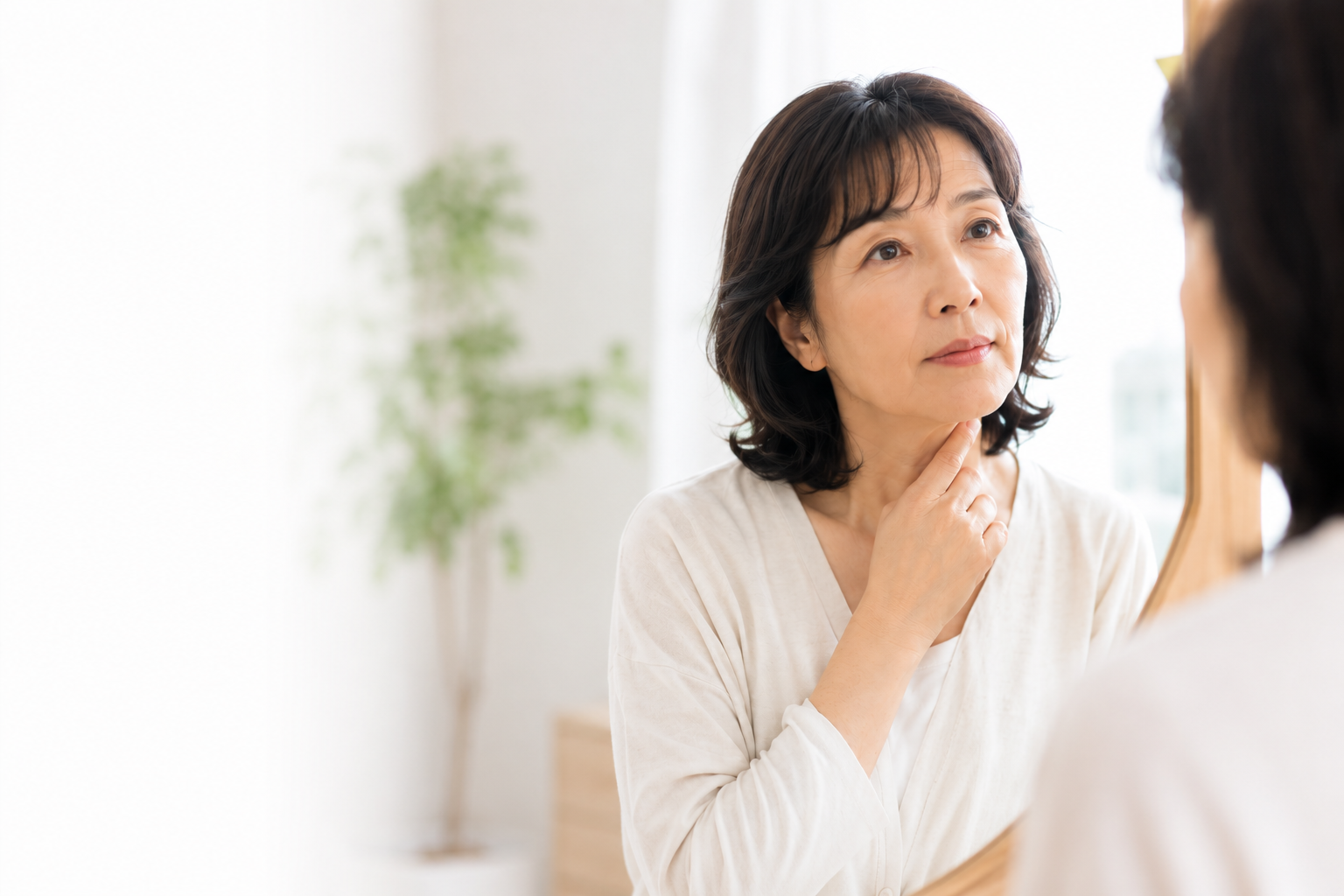 鏡を見ながら、のどのあたりを気にする女性